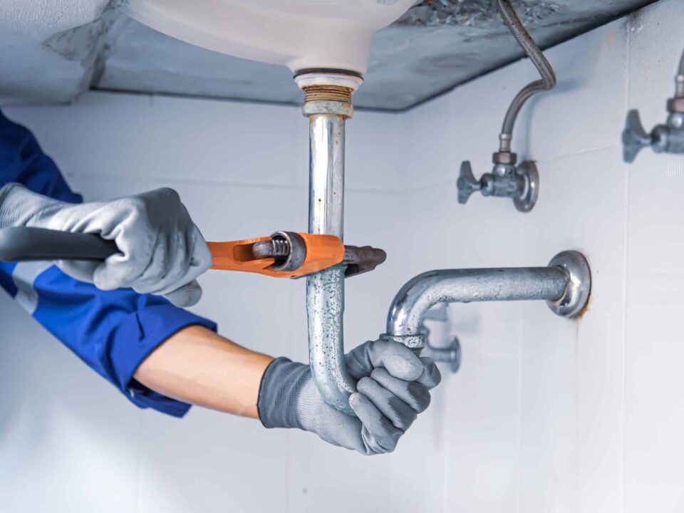 Technician plumber using a wrench to repair a water pipe under the sink. Concept of maintenance, fix water plumbing leaks, replace the kitchen sink drain, cleaning clogged pipes is dirty or rusty.